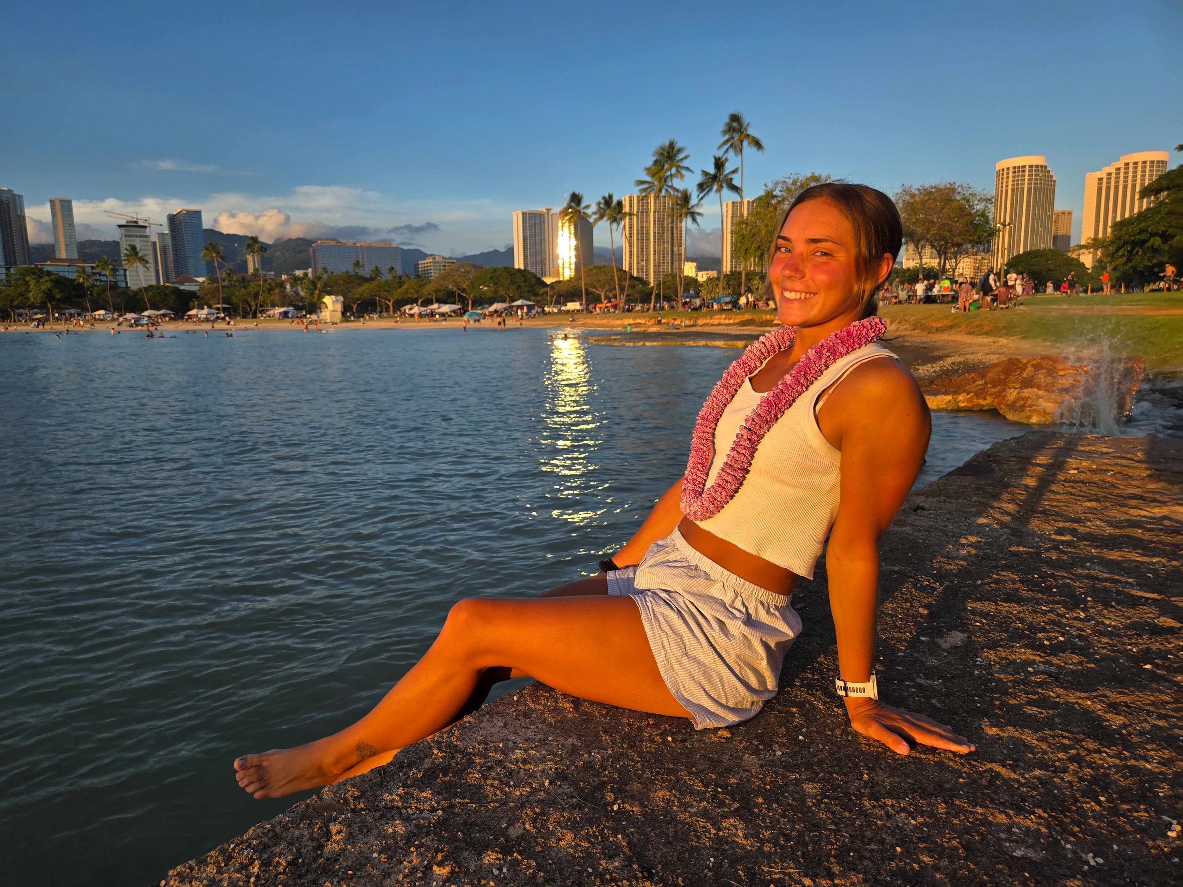 A girl in a carnation lei sitting at ala moana beach
