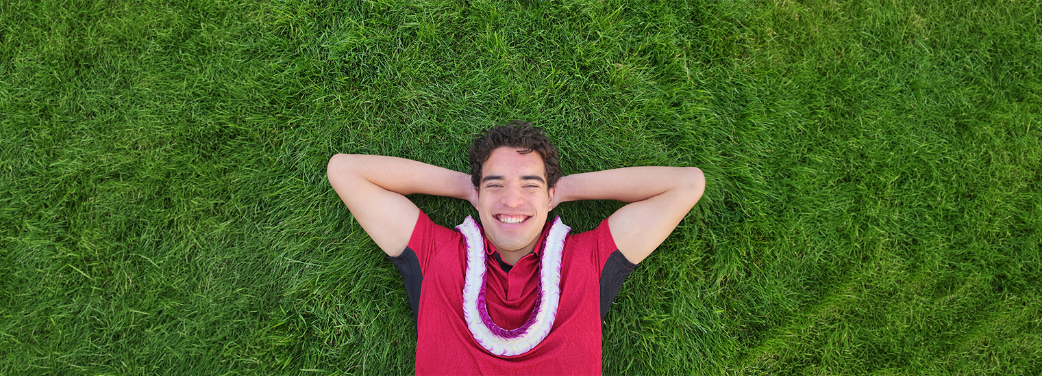 Guy lying in grass wearing a christina lei