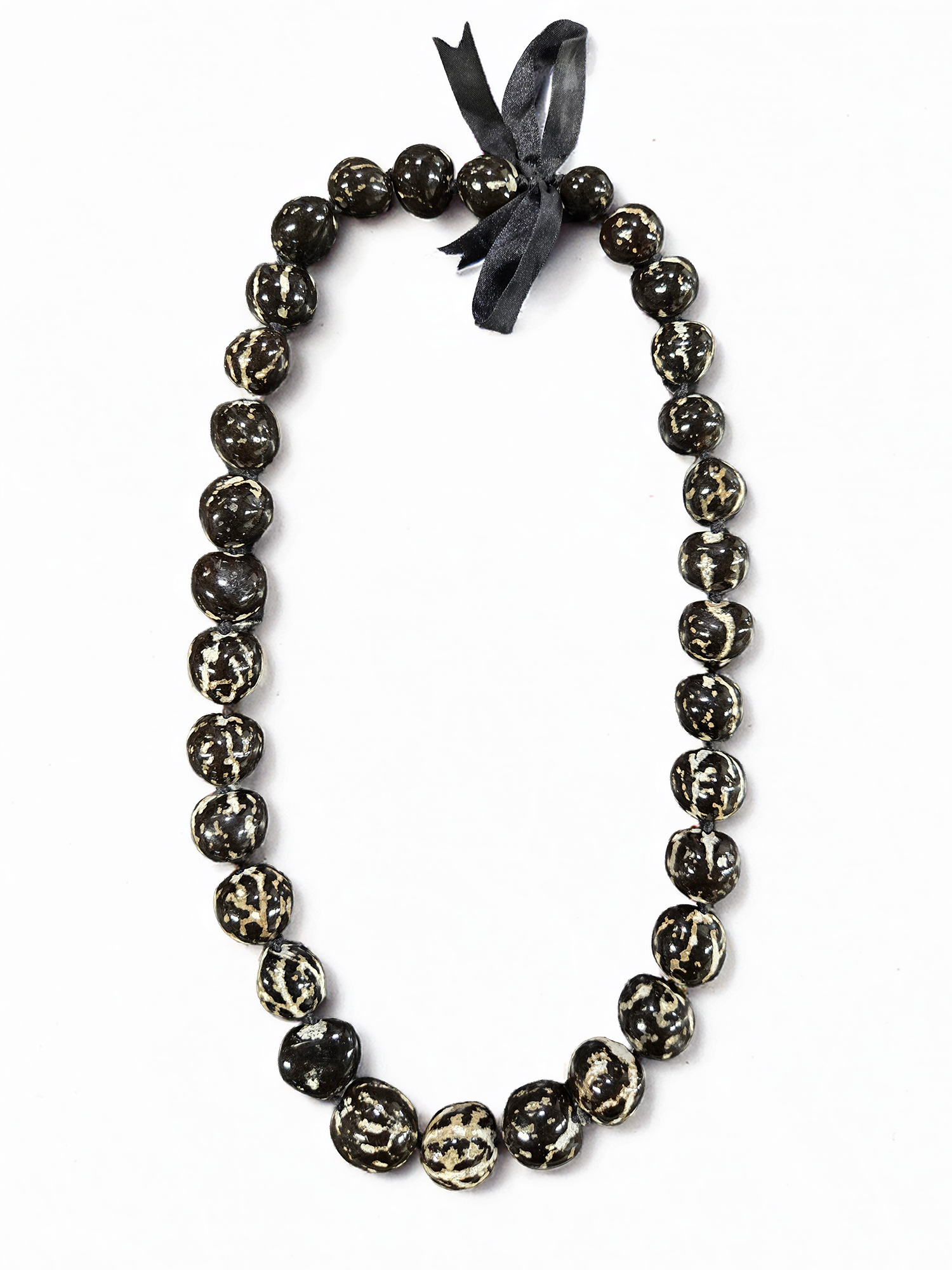 Tiger kukui nut lei with polished dark kukui nuts and cream marbled markings tied with a black ribbon on a white background